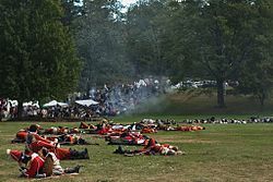 An open grassy area is strewn with bodies, most of them in red and 